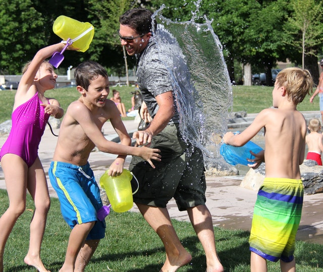 Kids in bathing suits use buckets to splash water on each other.