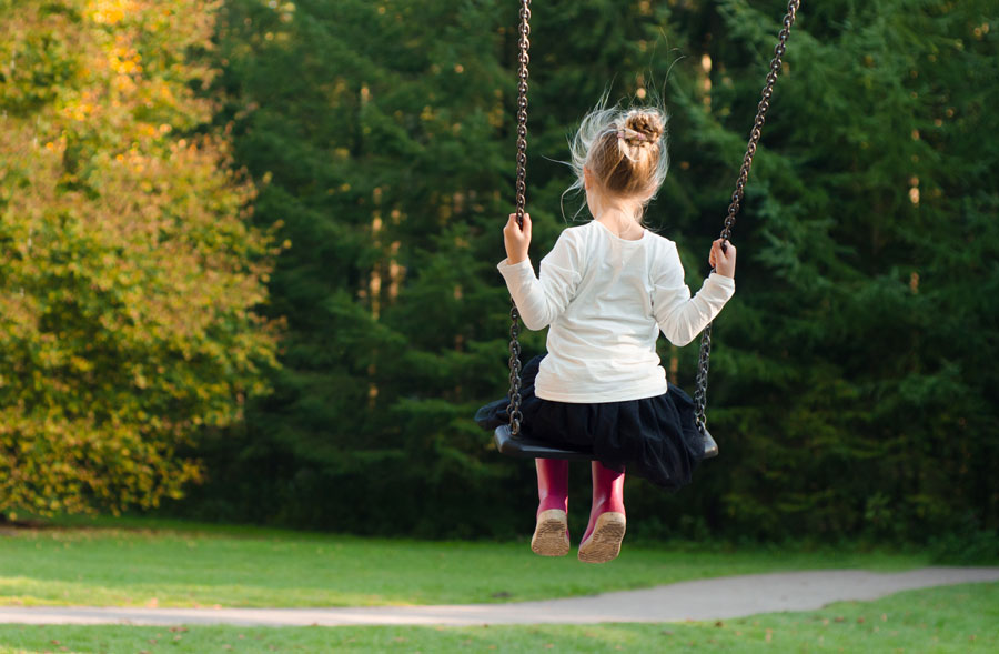 A young girl of around five sits on a swing- we see her from the back.