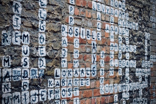 A mural on the side of a building has letters and words arranged like a crossword puzzle. In the center we see the word "possible."