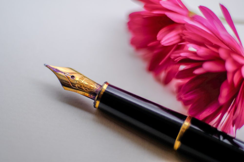 A close up of an ink pen and a pink flower