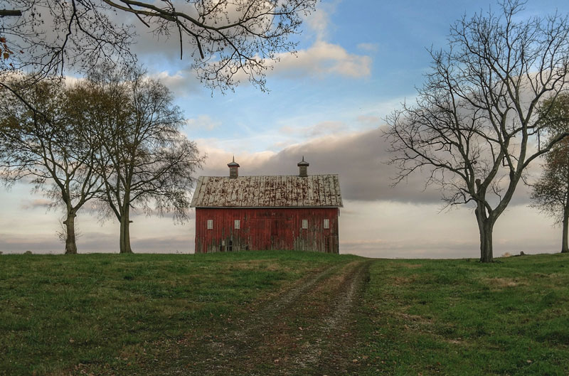 Landscape with red barn, bare trees and blue sky