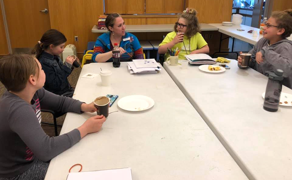 Five people work around a table while having a snack.