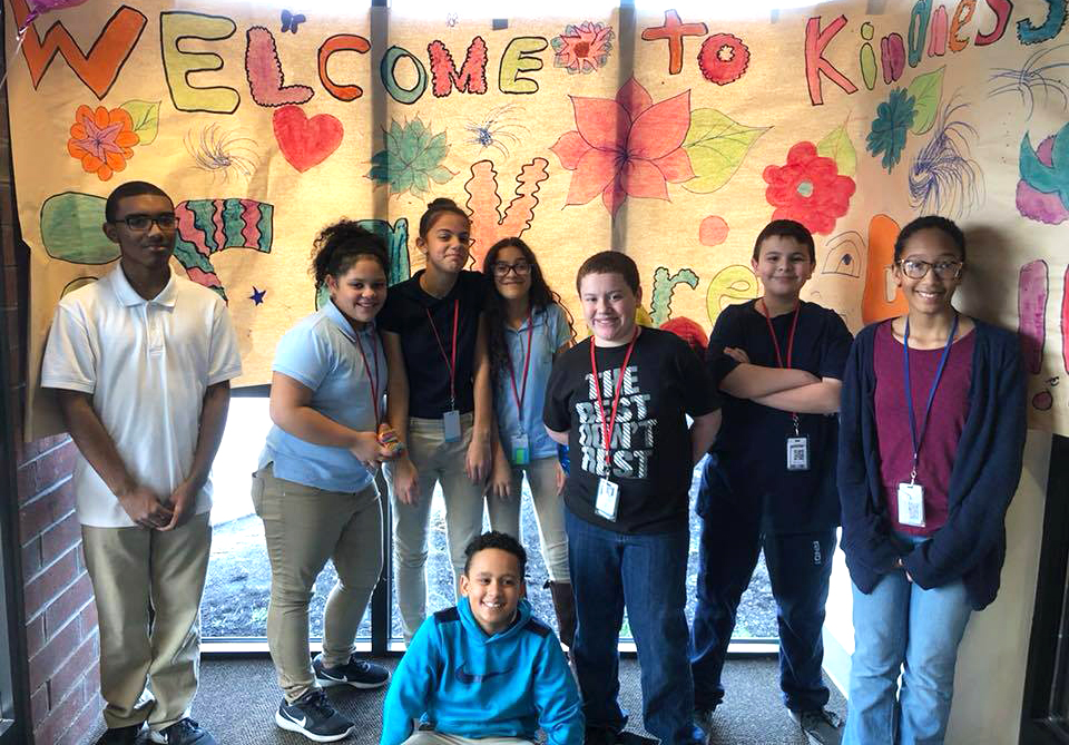 A group of middle school students pose in front of a homemade banner promoting kindness