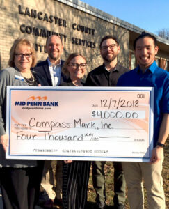 Four adults hold a giant check for $4,000 outside of the Lancaster County Community Services Center. They are grinning.