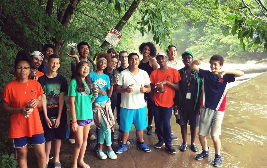 A group of tweens and teens pose in summer clothes in a wooded stream