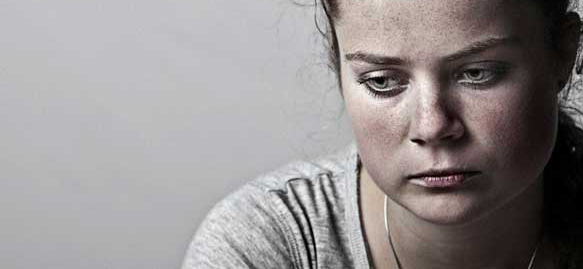 Close up of a young woman, wearing gray, looking down and to the left.