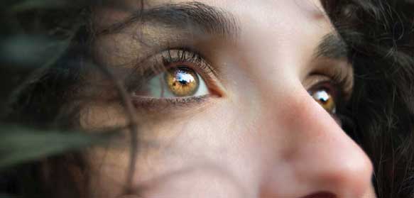 Extreme close up of young woman with dark, curly hair- just her eyes and nose, looking up