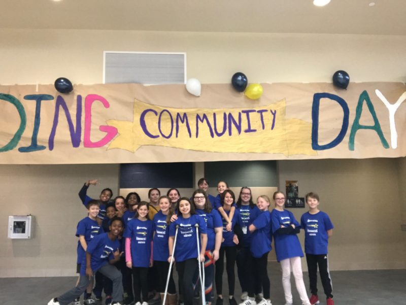 A group of middle school students in matching shirts stand in front of a huge banner reading "Building Community Day"