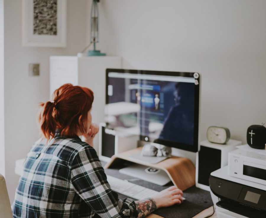 We see a young woman from behind in a home office. She's wearing casual clothes and her hair is in a messy pony tail.