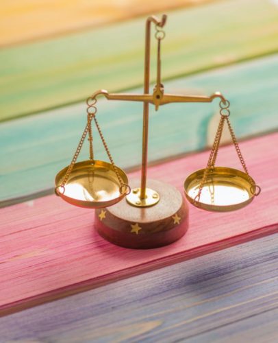 A shiny copper balance scale rests on wooden boards stained orange, green, blue, red and purple