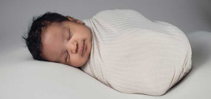Very new baby is sleeping and swaddled tightly in a white blanket