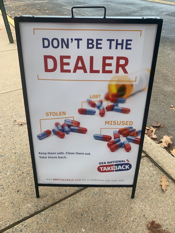 A sign outside on a sidewalk says "Don't Be the Dealer" with images of prescription medications.