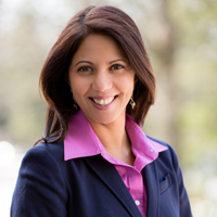 A woman in professional clothing is seen looking at the camera and smiling.