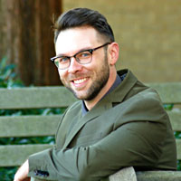 Man outside on a bench in business attire, smiling.