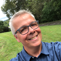 A man takes a closeup selfie outside- he is grinning.