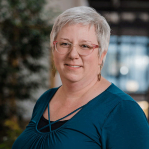 Headshot of woman in business casual clothing, in an indoor atrium, smiling