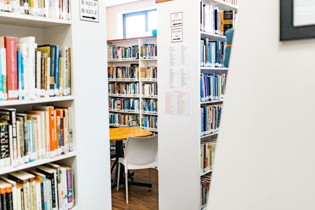 We see a corner of a library with colorful books on white shelves.