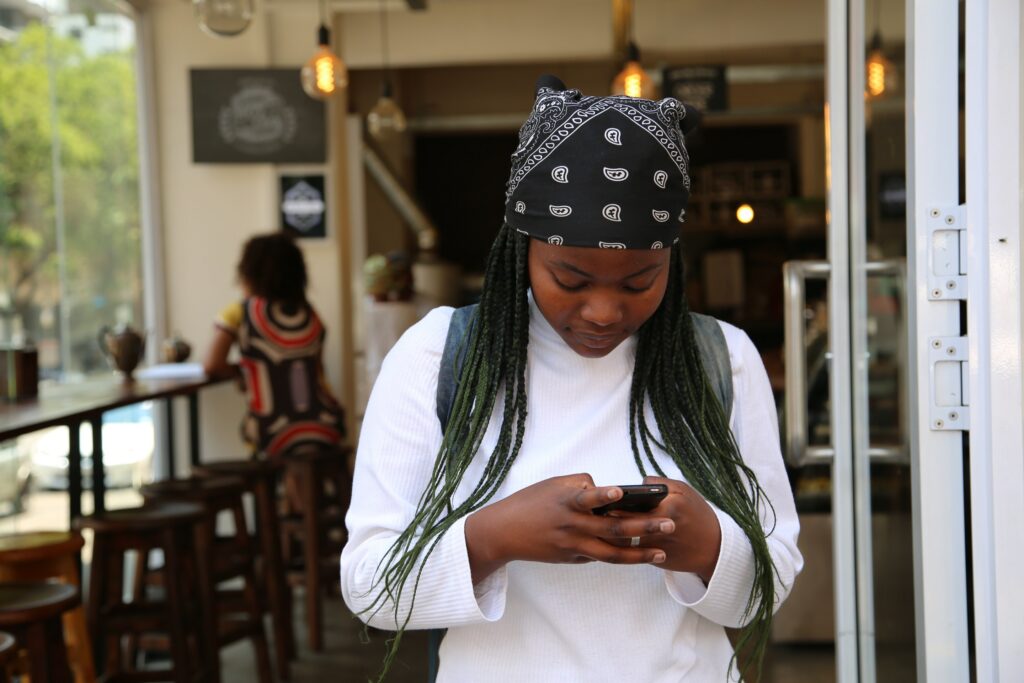 Looking into a cafe, a young woman in casual clothing is looking down at her phone, texting. 