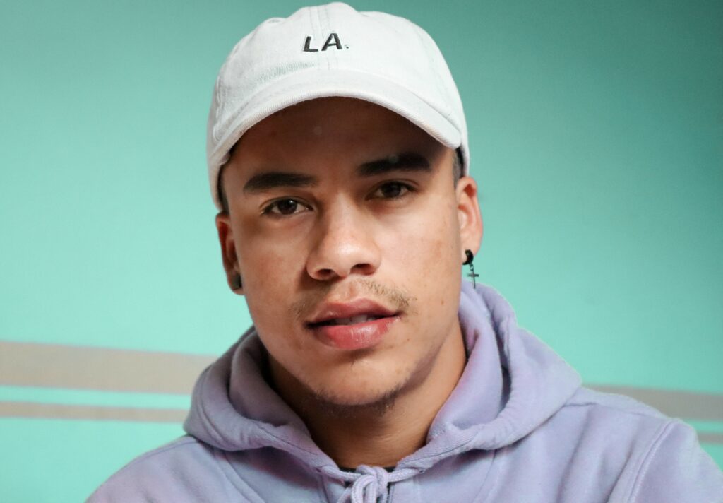 Headshot of a young man in a white baseball cap and gray hoodie