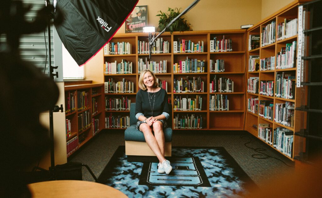 A woman is being interviewed in a home library with professional lights.