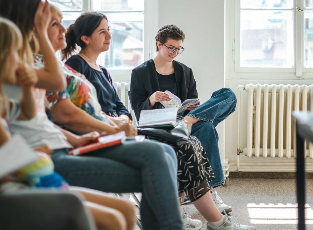 A group of people with notepads look up to the front of a room