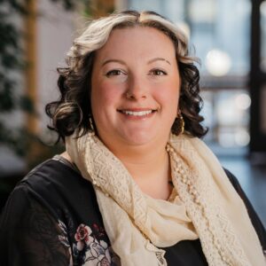 Headshot of a woman in flowered blouse and ivory scarf in an indoor atrium