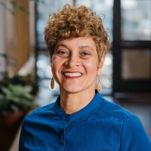 Headshot of a woman in business casual attire with plants and lots of windows