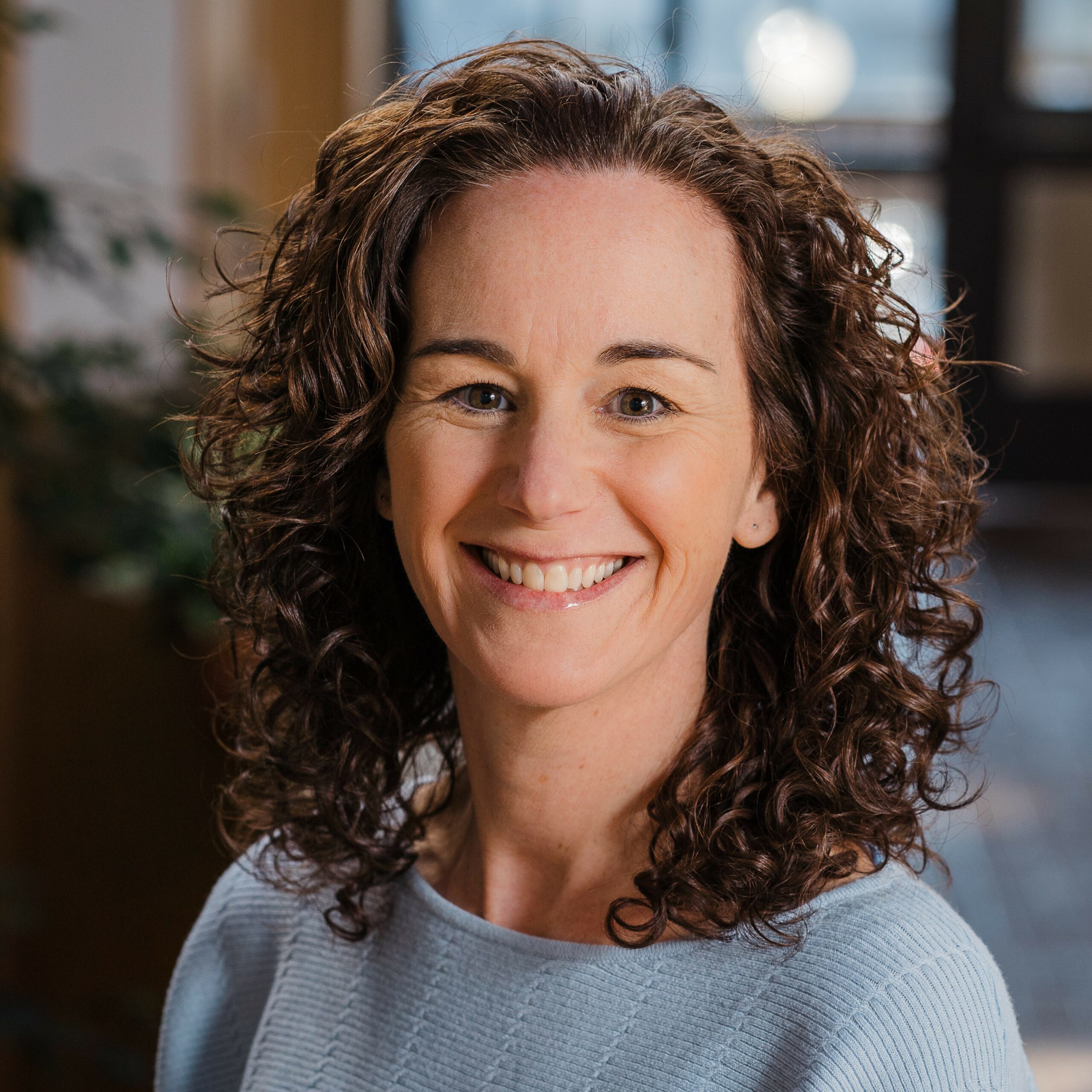 Headshot of a woman in business casual clothing in a plant-filled atrium