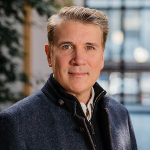 Headshot of a man in a smart jacket in an atrium with lots of light