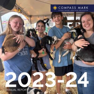 Photo of teenagers in matching shirts holding baby goats at a county fair. Text says, Compass Mark 2023-24 Annual report