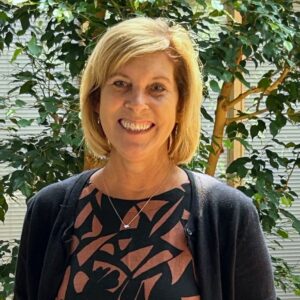 Headshot of a woman in business casual clothing in an atrium with indoor trees