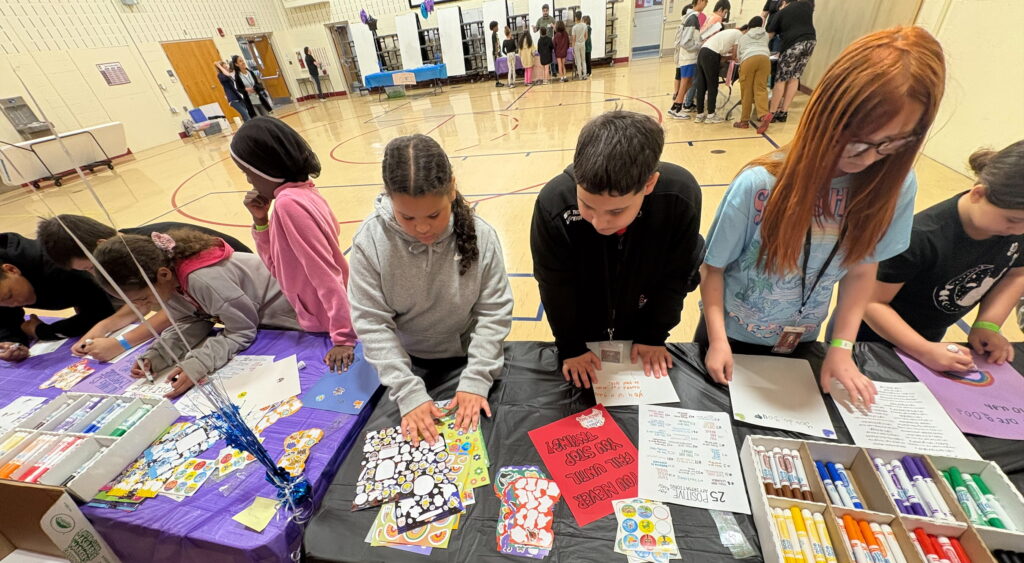 Middle school students line up at a table in the gym to make encouraging cards for family and friends