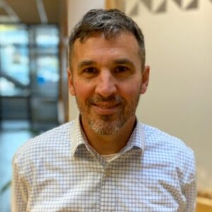 Headshot of a man in an indoor atrium in business casual clothing.