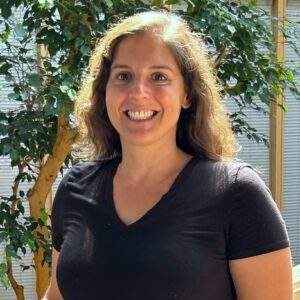 Headshot of a woman with fig trees in the background. She's in an indoor atrium.