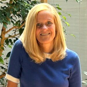 Headshot of a woman smiling in an indoor atrium with plants.