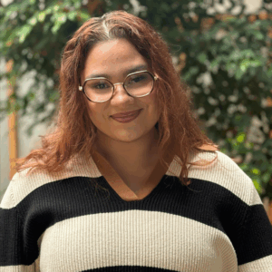 Headshot of a woman in business casual clothing in an indoor atrium with plants, smiling