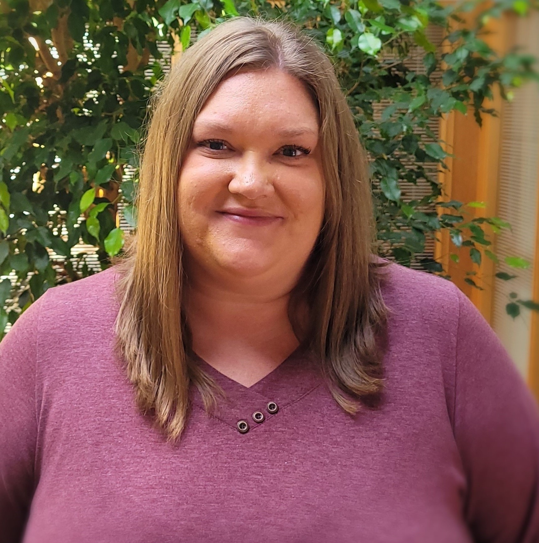 Headshot of a woman inside an atrium with tall plants.