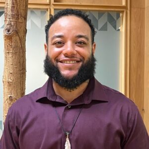 Headshot of man in indoor atrium with trees. He is smiling.