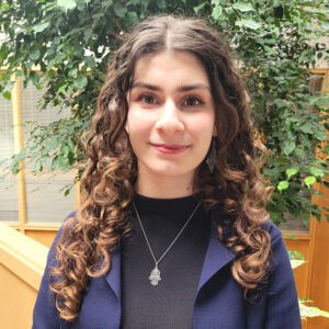 Headshot of a young woman in an inside atrium with trees.