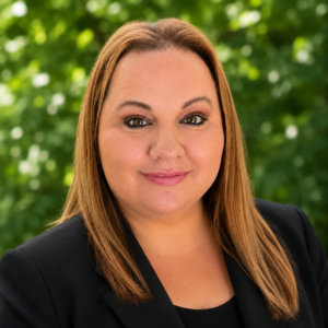 Headshot of a woman in business attire with greenery behind her.