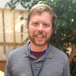 Headshot of a man with a lanyard inside an atrium that holds fig trees.
