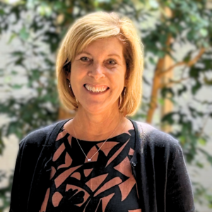 Headshot of a woman in business casual clothing in an atrium with indoor trees