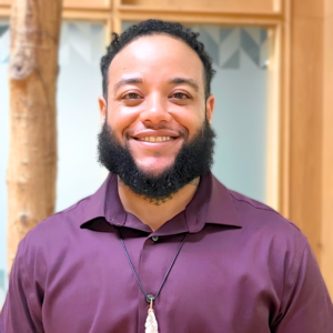 Headshot of man in indoor atrium with trees. He is smiling.