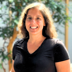 Headshot of a woman with fig trees in the background. She's in an indoor atrium.