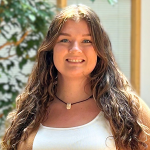 Headshot of a young woman smiling in an inside atrium with plants