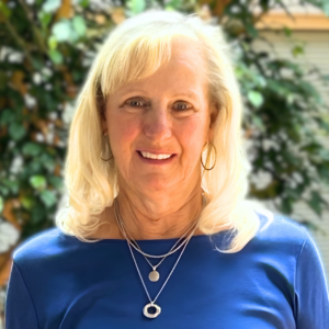 Headshot of a woman in an indoor atrium with fig trees. She is smiling.